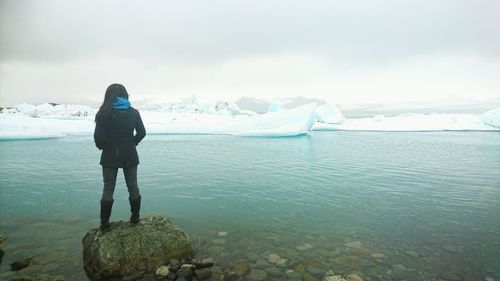 Rear view of woman standing on lakeshore at jokulsarlon lagoon