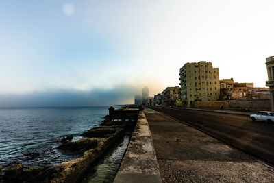 Road by sea and buildings against sky