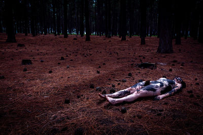 Naked woman covered with paint while lying down in forest