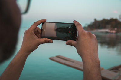 Cropped hands of man photographing lake with smart phone