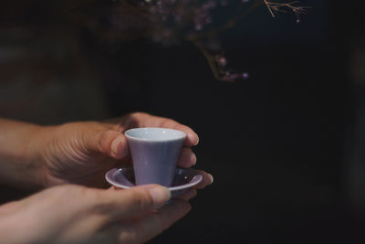 Close-up of hand holding coffee cup against black background