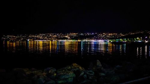 Illuminated buildings by sea against sky at night