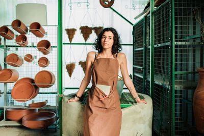 Portrait of smiling young woman standing against wall in workshop