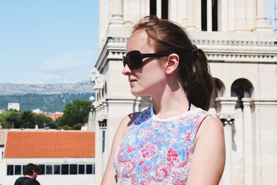 Portrait of woman wearing sunglasses standing against built structure