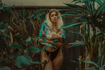 Seductive woman standing amidst plants at backyard