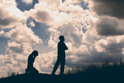 Silhouette couple on field against cloudy sky