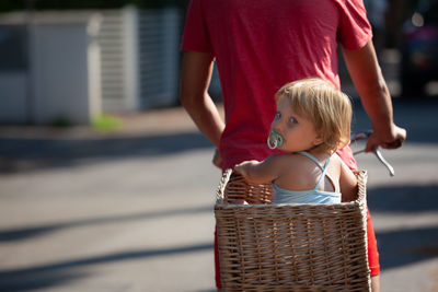 Midsection of father with daughter in wicker basket riding bicycle on street