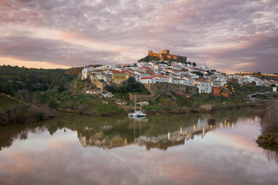 Buildings by lake against cloudy sky