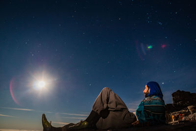 Rear view of people sitting against sky at night