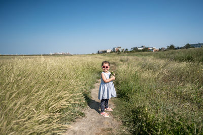 Full length portrait of girl standing on field against sky