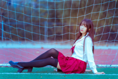 Portrait young woman sitting against net on soccer field