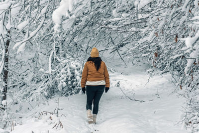 Rear view of girl wearing winter clothes, walking on snowy path in forest