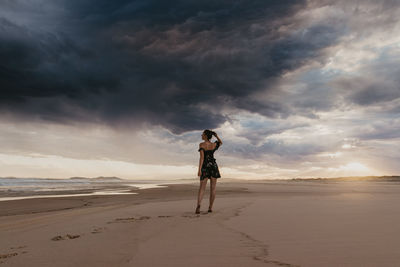 Rear view full length of young woman standing at beach during sunset