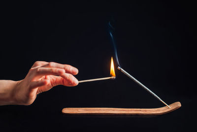 Hand with a match igniting an incense stick in a holder, black background