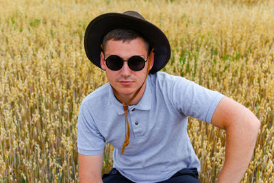 Man in sunglasses. portrait of farmer seating in gold wheat field with blue sky in background. young