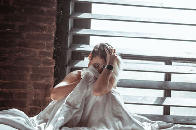 Portrait of young woman with blanket on bed sitting against window