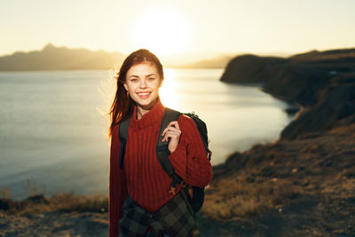 Portrait of smiling young woman standing at beach during sunset
