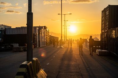 Silhouette people on street against sky at sunset