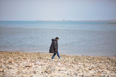 Rear view of man standing at beach against sky