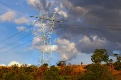 Low angle view of electricity pylon on land against cloudy sky