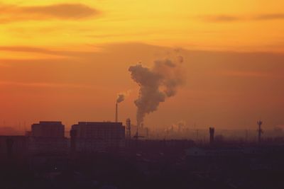 Smoke emitting from factories against sky during sunset