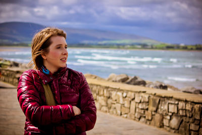 Young woman standing at beach against sky