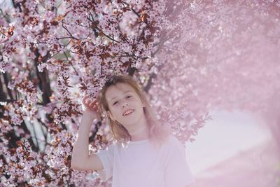 Portrait of young woman standing amidst cherry blossom tree