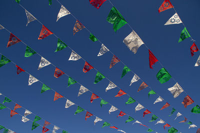 Low angle view of multi colored flags hanging against blue sky