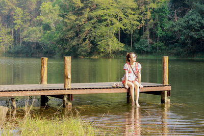 Boy sitting by lake against trees