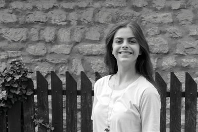 Portrait of smiling young woman standing against wall