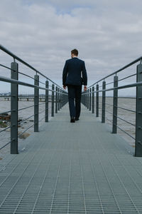 Rear view of businessman walking on pier over sea against sky