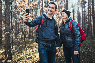 Couple taking selfie photo while vacation trip. hikers walking on path in forest on sunny day