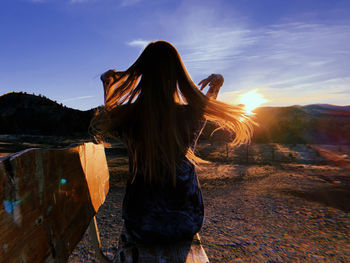 Rear view of woman sitting on bench against sky during sunset