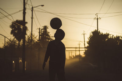 Silhouette man standing by electricity pylon against sky during sunset
