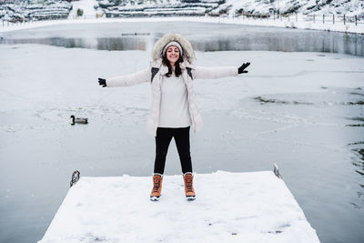 Happy caucasian woman with eyes closed and arms outstretched standing on snowy pier during winter