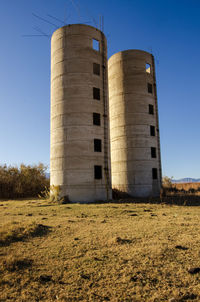 Low angle view of concrete silos on field against clear blue sky
