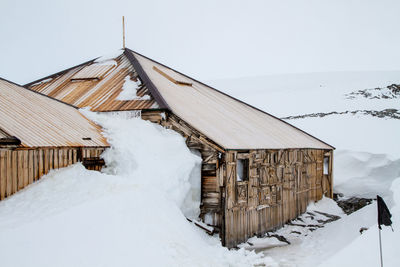 Snow covered cottage by building against clear sky