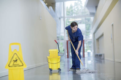 Male worker cleaning floor at hospital corridor