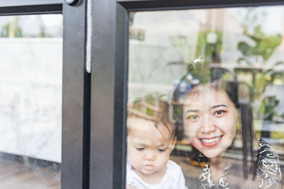 A mother-daughter family with a small daughter in the house, photographed through the glass.