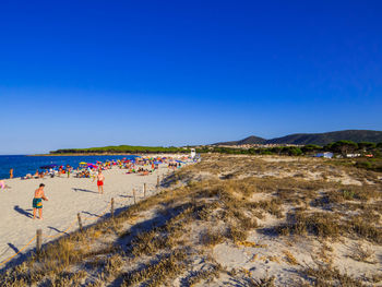 People at beach against clear blue sky