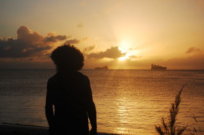 Rear view of silhouette boy standing at beach during sunset