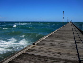 Pier over sea against clear blue sky