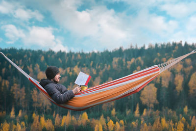 Man reading book while relaxing in hammock against trees