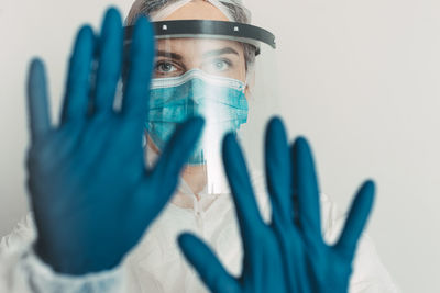 Portrait of female doctor wearing face shield and mask gesturing against gray background
