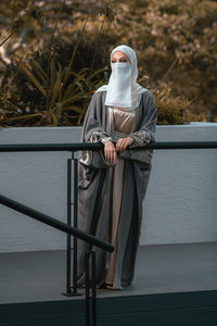 Full length picture of veiled woman with white niqab and hijab standing by railing