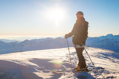 Adult girl on skis stands on a mountainside, admiring the mountain landscape, looking at the camera