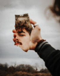 Close-up of man holding mirror with reflection against sky