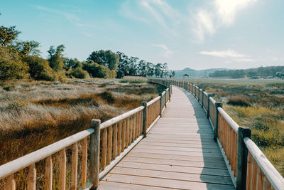 View of wooden footbridge on landscape against sky