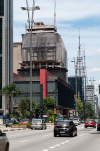 Cars on road by buildings in city against sky