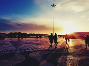 Silhouette men on road against sky during sunset